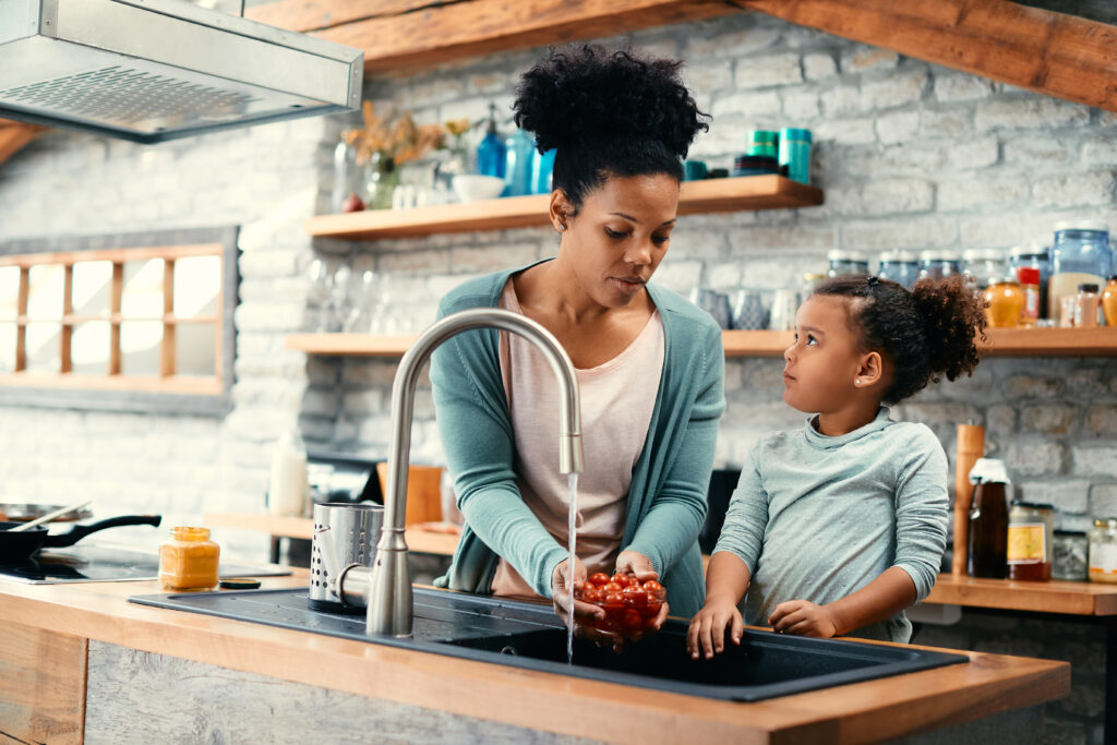 Mother and daughter cleaning vegetables in sink